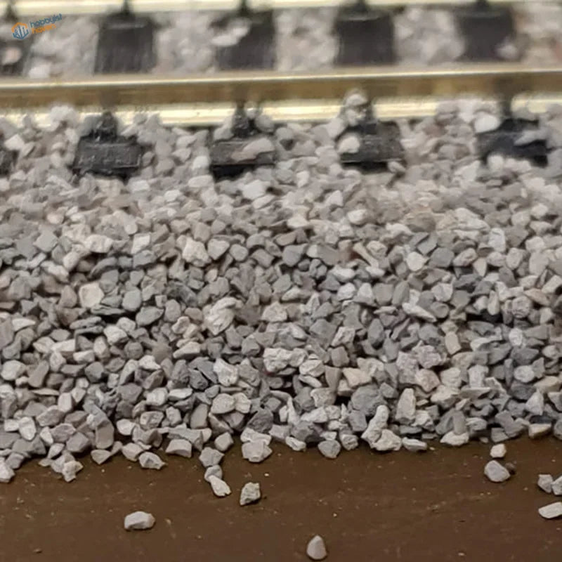 100g ballast gravel bag with textured gray gravel under miniature train tracks