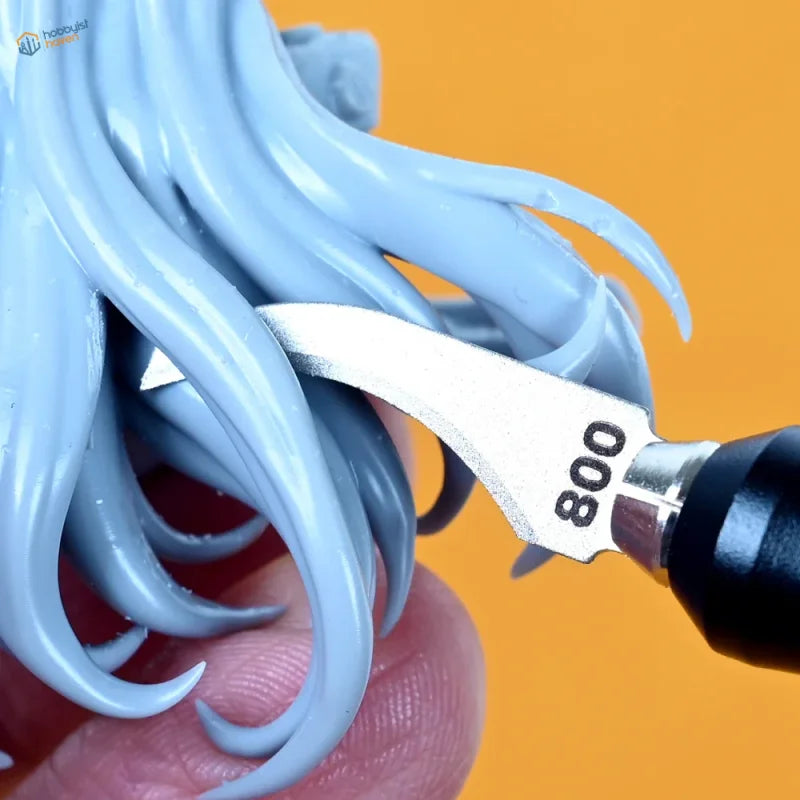 A silver 800-grade sculpting knife with black handle used as a curved emery file blade on light blue plastic hair