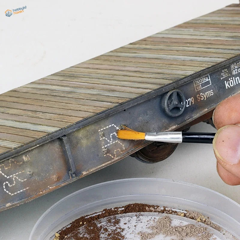 Double-headed weathering brush applying paint to miniature train car rust