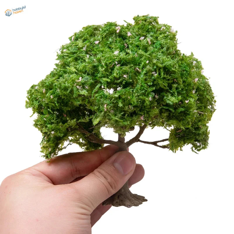 Hand holding 150mm model tree with mossy green foliage and white blossoms for dioramas, precision hobby tools
