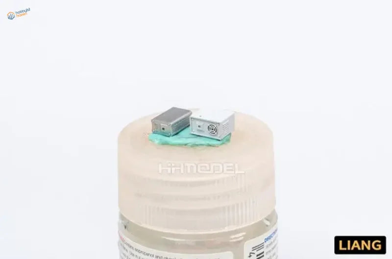 Two 3D-printed 1/35 model storage battery components on beige paint bottle lid