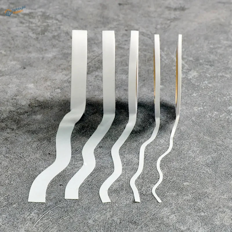Five white wavy flexible masking tape strips in a row on gray surface