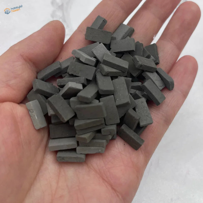 A hand holds a pile of small dark gray ceramic miniature bricks for diorama scenery and scale modeling tools