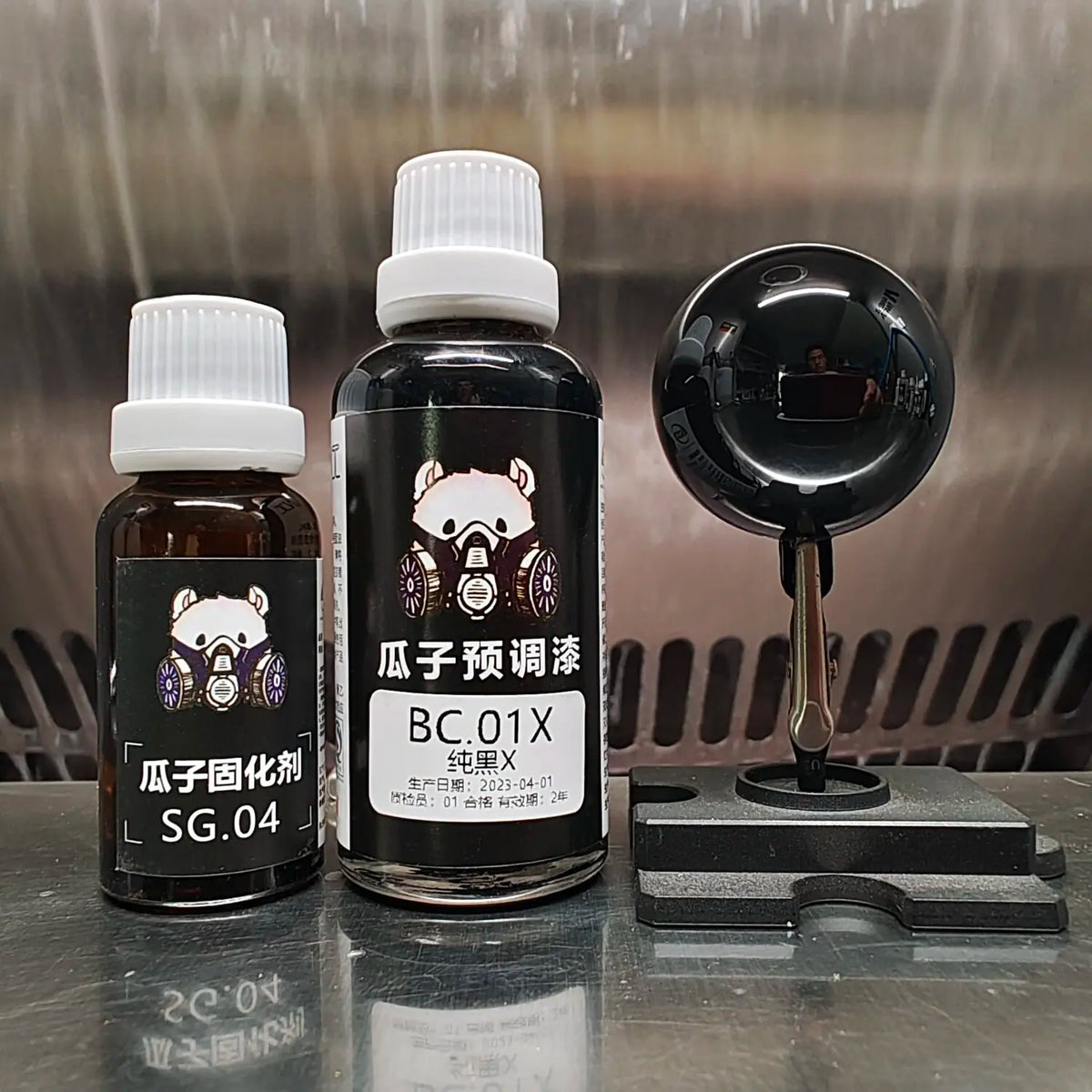 Guazi BC.01X gloss black paint bottle and hardener bottle beside a mirror-black painted sphere