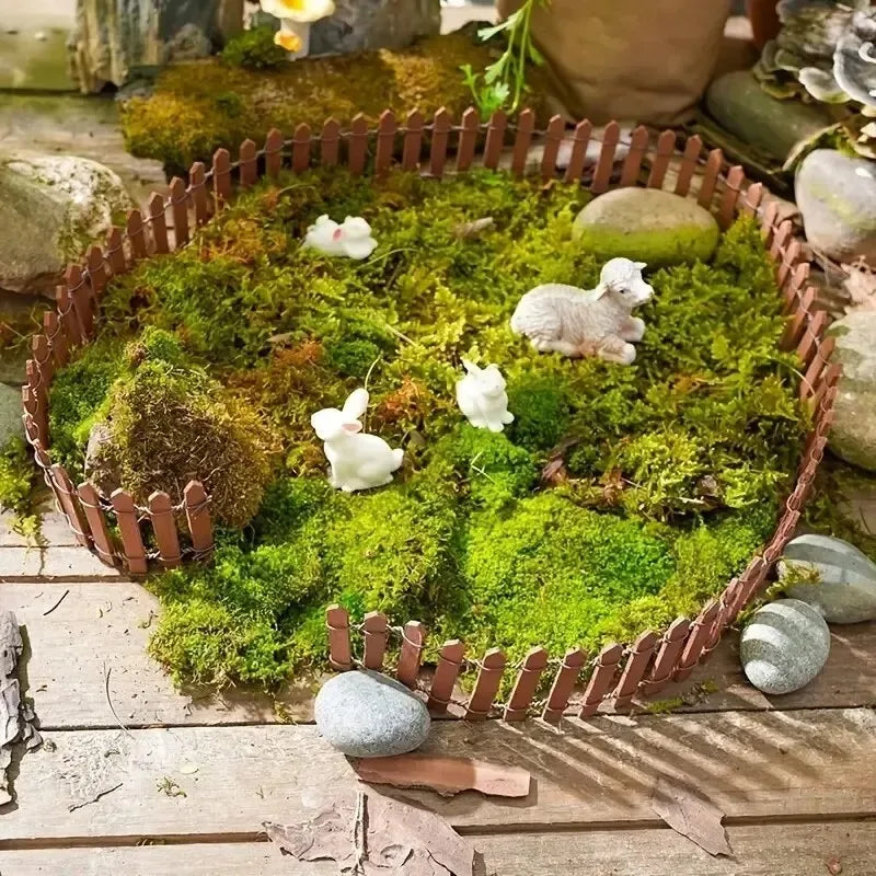 Miniature wooden picket fence in brown enclosing green moss with white ceramic rabbits and sheep for garden decoration