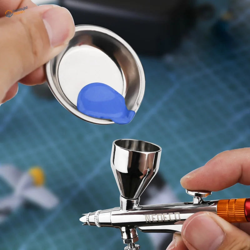 Silver orange airbrush sprayer with neelo engraving filled from blue paint cup in assorted accessories set