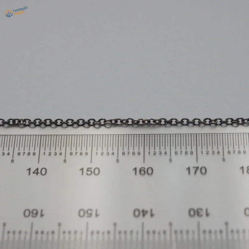 A sleek black metal anchor chain with consistent oval links lying across a ruler for model ships use