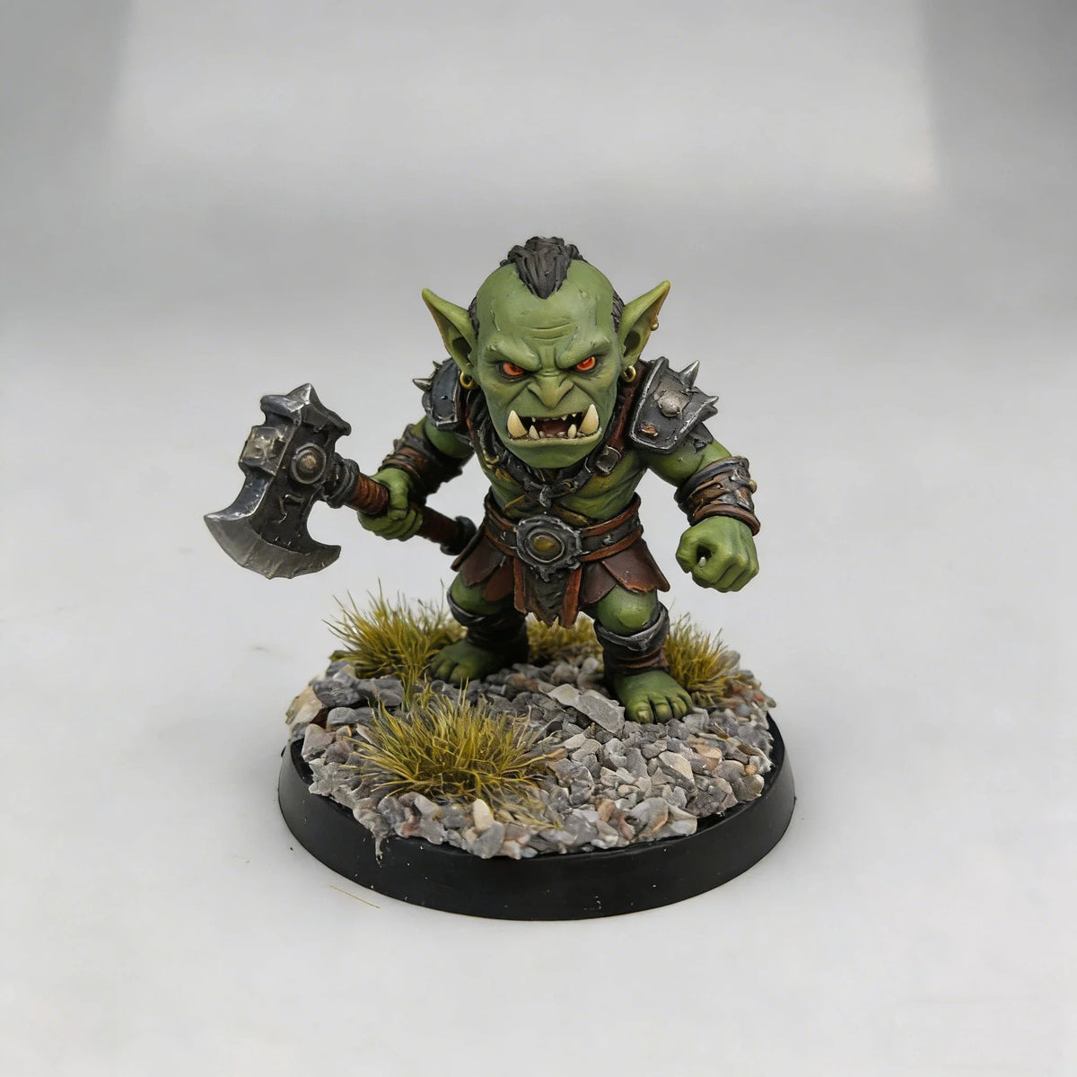 Green-skinned orc miniature with orange eyes on scenic base toppers featuring gravel and grass for scale modeling tools