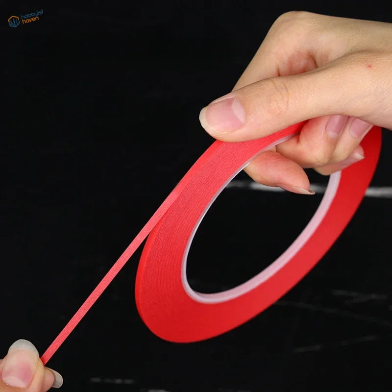 Red fine line masking tape for scale modeling with a thin flexible strip being pulled from the roll for model building tools