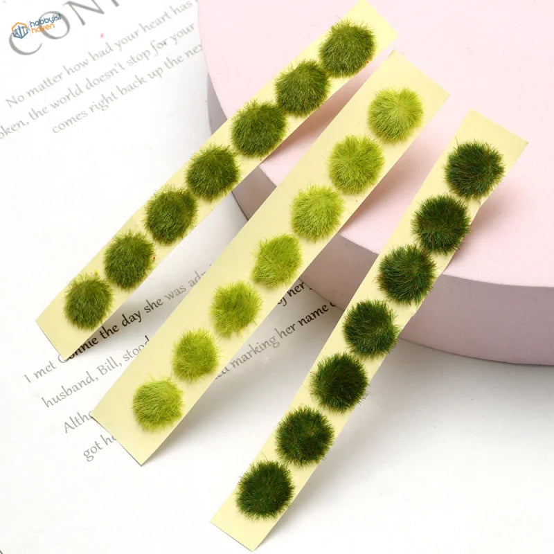 Back of green miniature flower clusters with fuzzy moss balls on yellow adhesive