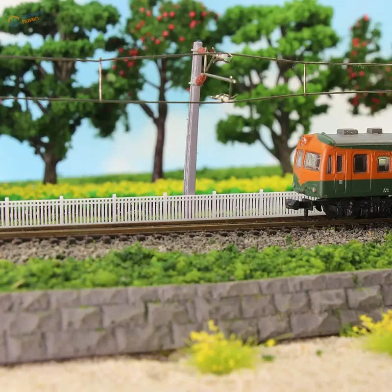 N scale white lattice-top picket fence wall in 1 meter three pieces displayed near orange and green model train