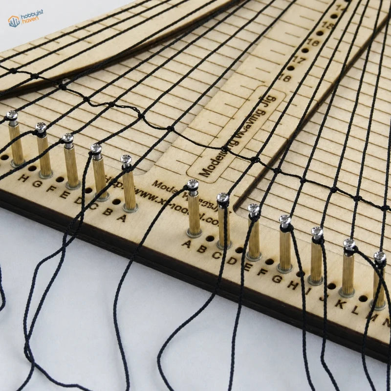 Beige wooden rope ladder weaving jig with black cord threaded through gold pegs and labeled measurement markings