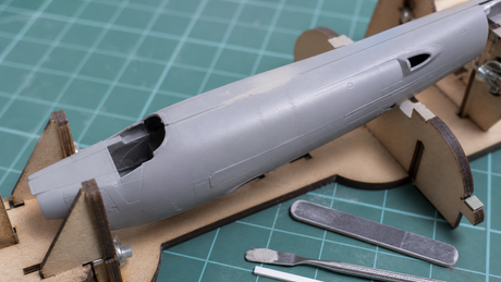 Filled and sanded center seam on a gray plastic scale model aircraft fuselage held in a modeling jig.