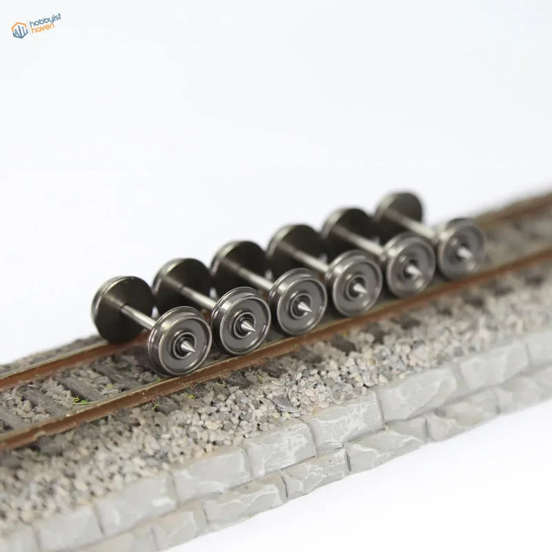A set of six 1/87 HO scale metal train wheels with metallic silver finish and detailed axles on miniature railway track