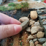 Hand holding smooth grayish-brown 100ml miniature rock, 4 rock sizes