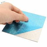 Back of 100mm x 100mm aluminum plate with blue peel-off sticker on silver surface
