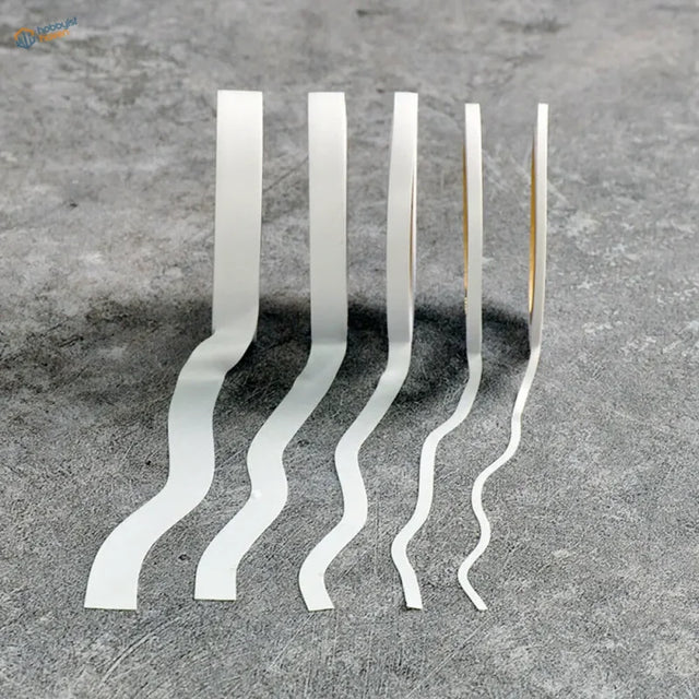 Five white wavy flexible masking tape strips in a row on gray surface