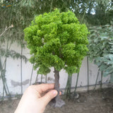 Hand holding 22-30cm artificial tree for scale modeling with green moss foliage