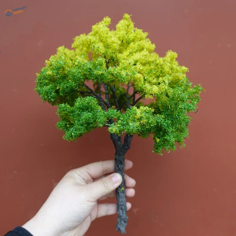 Hand holding 22-30cm artificial tree for scale modeling, dark trunk and vibrant foliage