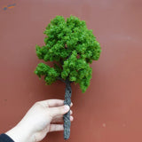 Hand holding 22-30cm artificial tree for scale modeling with mossy green foliage