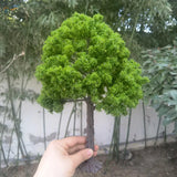 Hand holding 22-30cm artificial tree for scale modeling with mossy green foliage