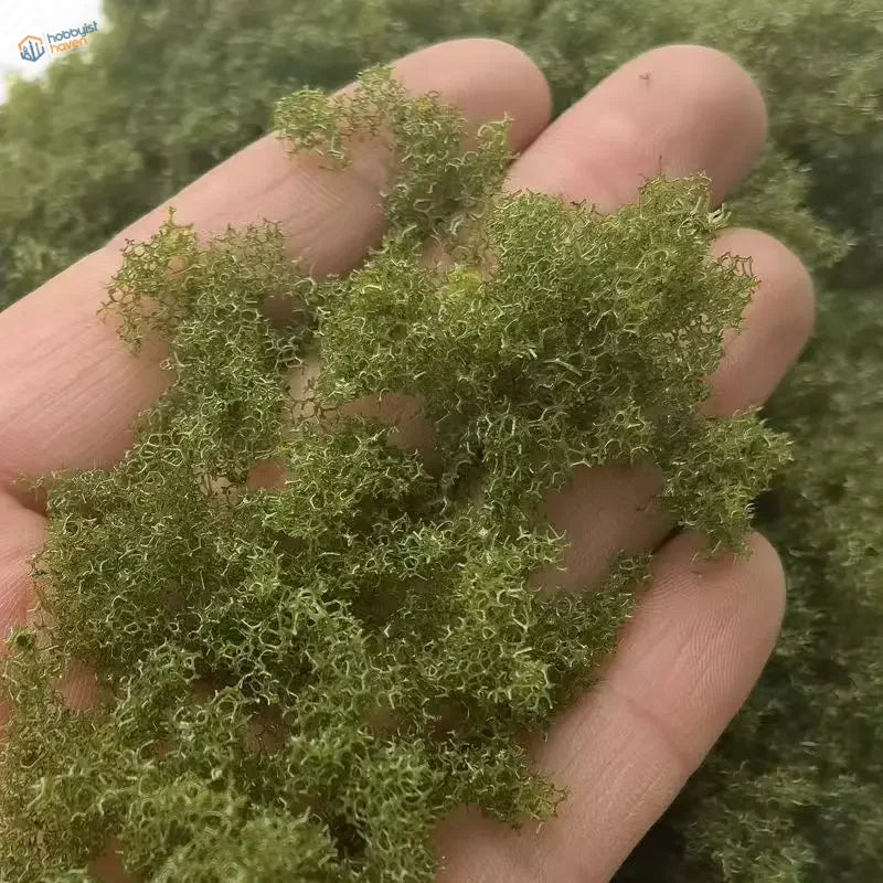 Hand holding 22g Green Tree Powder moss for scale modeling tools