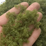 Hand holding 22g Green Tree Powder moss for scale modeling tools