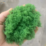 Hand holding 22g Green Tree Powder, vibrant green fluffy moss for scale modeling tools
