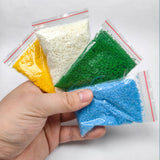 Four clear plastic bags with colored granular crushed coal in a nine-piece scenery starter pack for diorama scenery