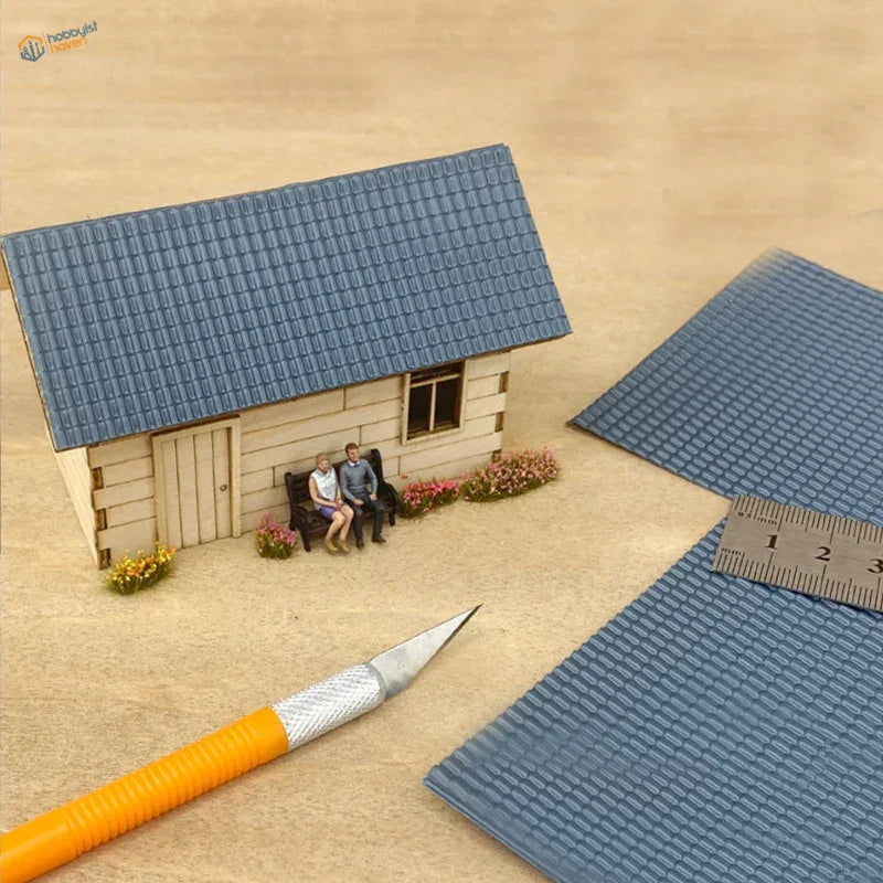 Miniature house with blue roof simulating PVC panels, beige siding, tiny figurines on bench