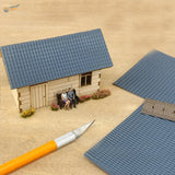 Miniature house with blue roof simulating PVC panels, beige siding, tiny figurines on bench