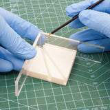 Multi-angle gluing jig with clear acrylic ruler and beige base being painted by gloved hands for scale modeling tools