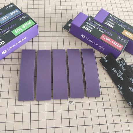 Five purple ultra-thin 2mm sanding sponge strips laid out on a cutting mat next to boxes of 400 to 1500 grit strips