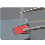 Decal tweezers with a long pointed tip hovering over a decal on a grey model part