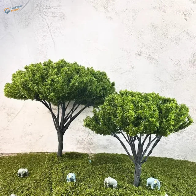 Two African model trees with white elephant figurines on grass