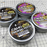 Silver tin containers of soft-edge camouflage masking putty in black and blue-green for effective camouflage masking