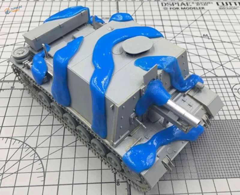 Gray plastic tank model with blue camouflage masking putty flows