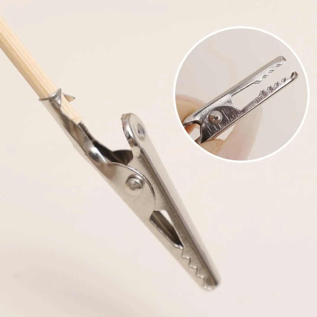 Silver alligator clip with serrated jaws gripping wooden stick, model building tool