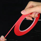 Red fine line masking tape for scale modeling with a thin flexible strip being pulled from the roll for model building tools
