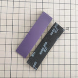 Close-up of a purple sanding sponge strip next to a black #600-800 grit strip on a cutting mat