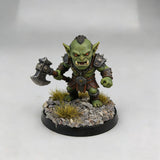 Green-skinned orc miniature with orange eyes on scenic base toppers featuring gravel and grass for scale modeling tools