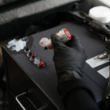 Gloved hand holds dark red tattoo ink bottle for precision hobby tools