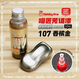 A 50ml bottle of Hobby Mio oil-based metallic paint in champagne gold with silver cap and gold label for precision hobby tools