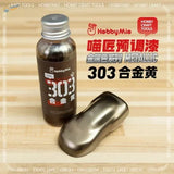 A bottle of Hobby Mio 50ml oil-based metallic paint in 303 gold with a silver cap next to a golden swatch for scale modeling tools