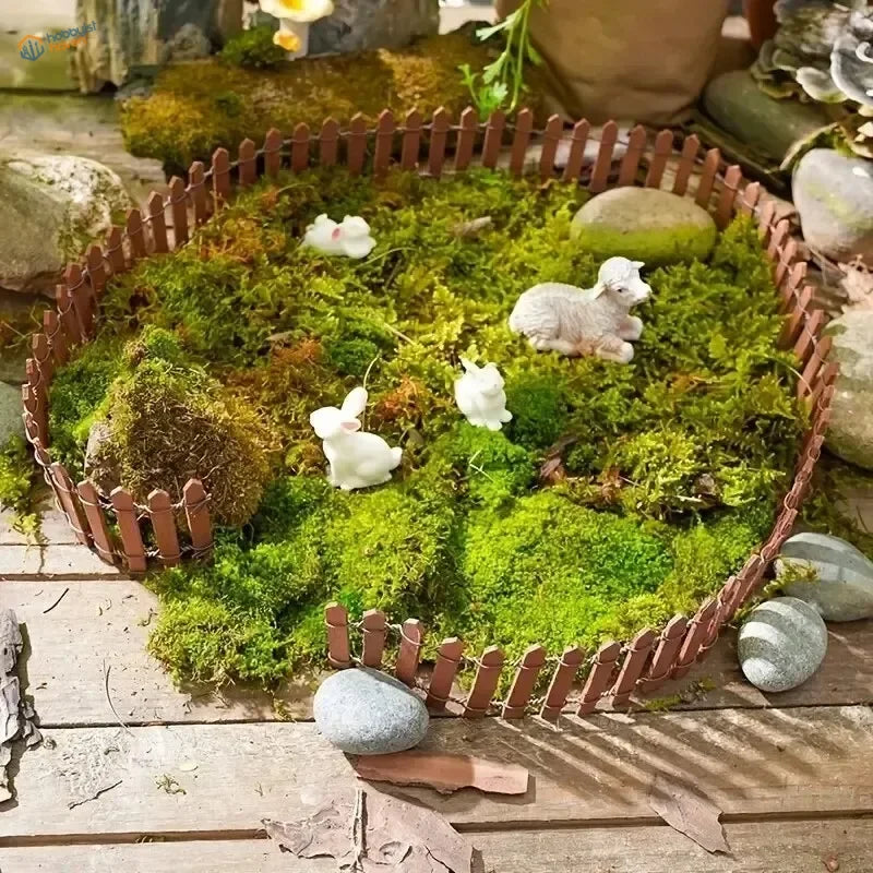 Miniature wooden picket fence in brown enclosing green moss with white ceramic rabbits and sheep for garden decoration