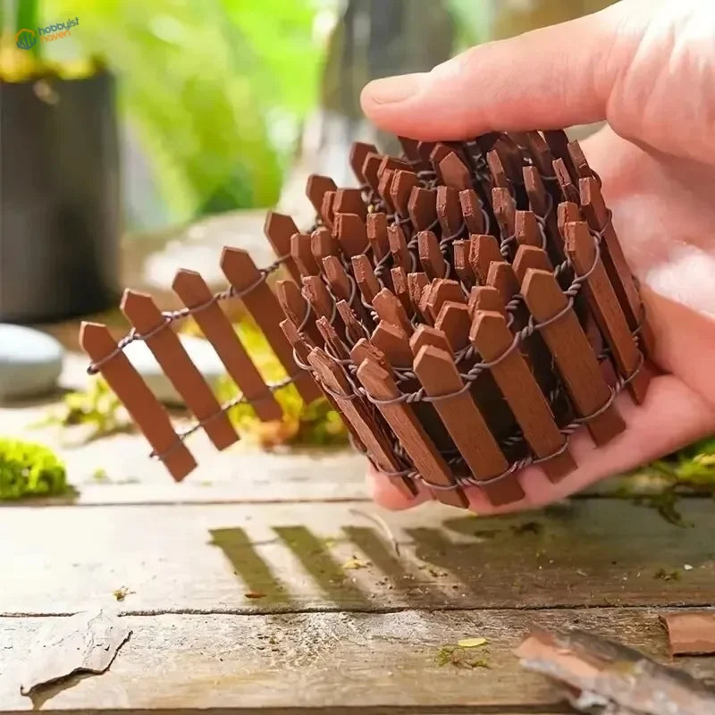 A compact brown wooden picket fence with pointed pickets and wire mesh for miniature garden and diorama decoration