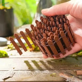 A compact brown wooden picket fence with pointed pickets and wire mesh for miniature garden and diorama decoration