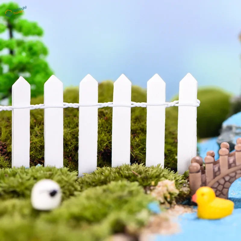 Miniature wooden picket fence with white pointed tops and twisted wire railing on mossy ground for garden decoration