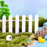 Miniature wooden picket fence with white pointed tops and twisted wire railing on mossy ground for garden decoration