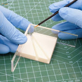 Multi-angle gluing jig with clear acrylic ruler and beige base being painted by gloved hands for scale modeling tools